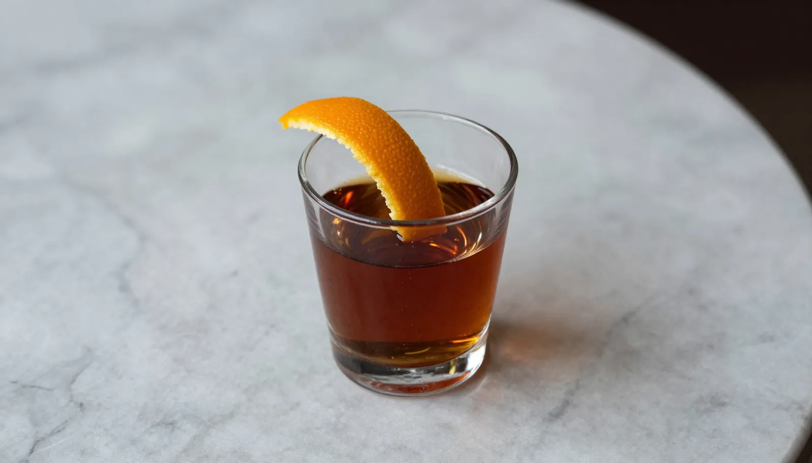 Ly amaro sẫm màu với vỏ cam trên bàn đá cẩm thạch