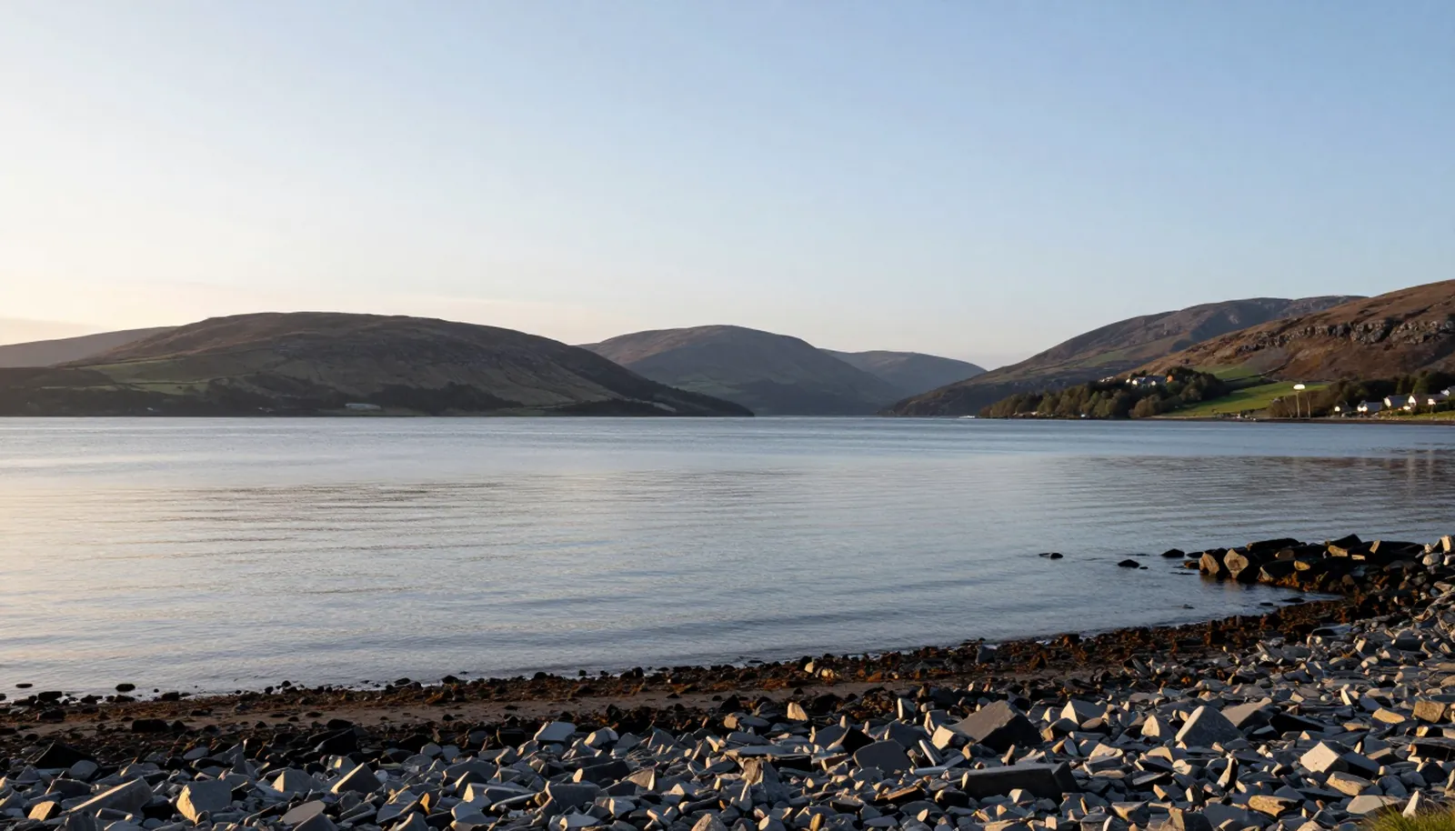 Mặt nước vịnh lặng với đồi thấp và bờ đá ở cao nguyên Scotland