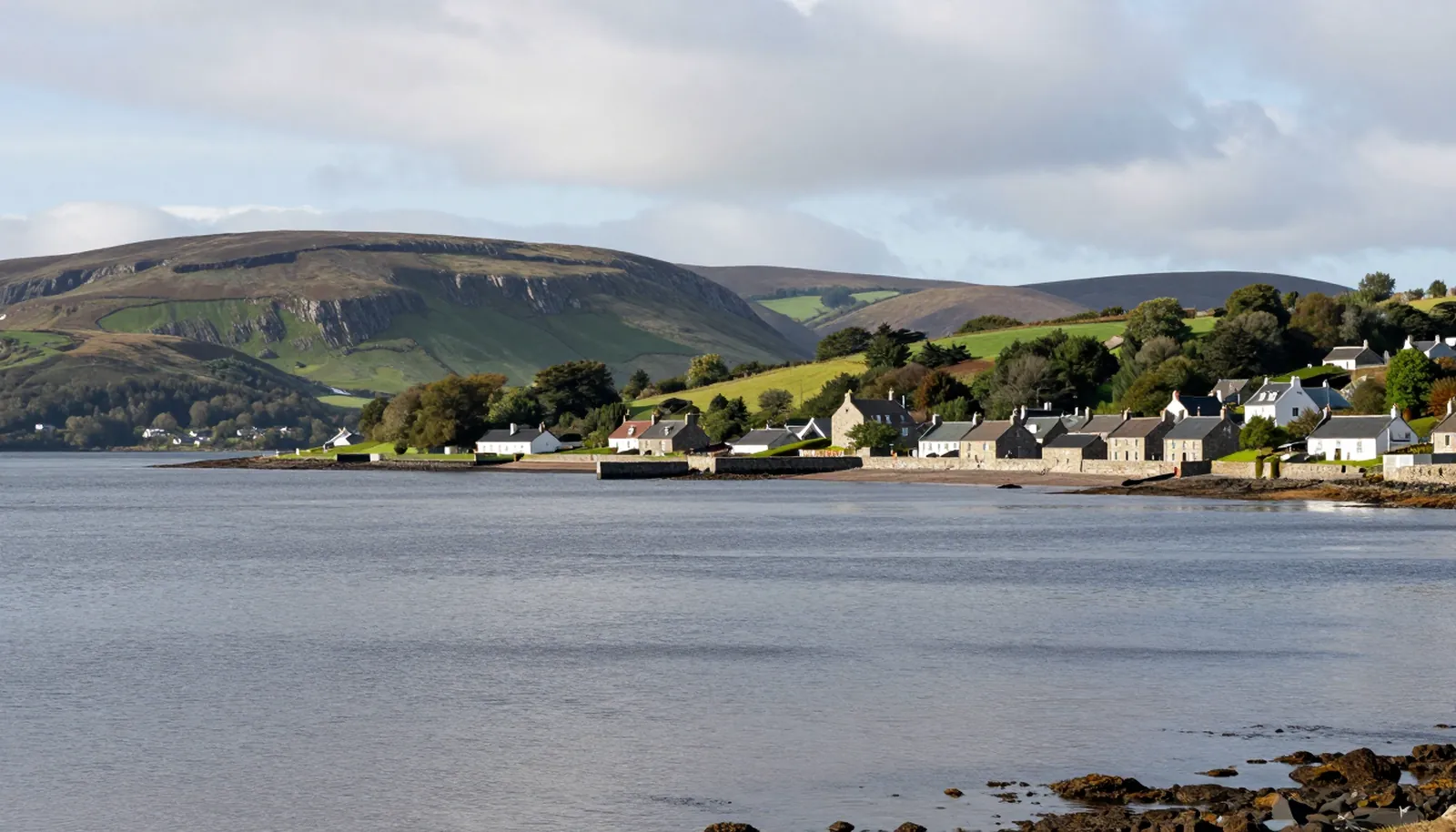 Cửa sông phẳng lặng với đồi xanh và thị trấn đá nhỏ ở miền bắc Scotland