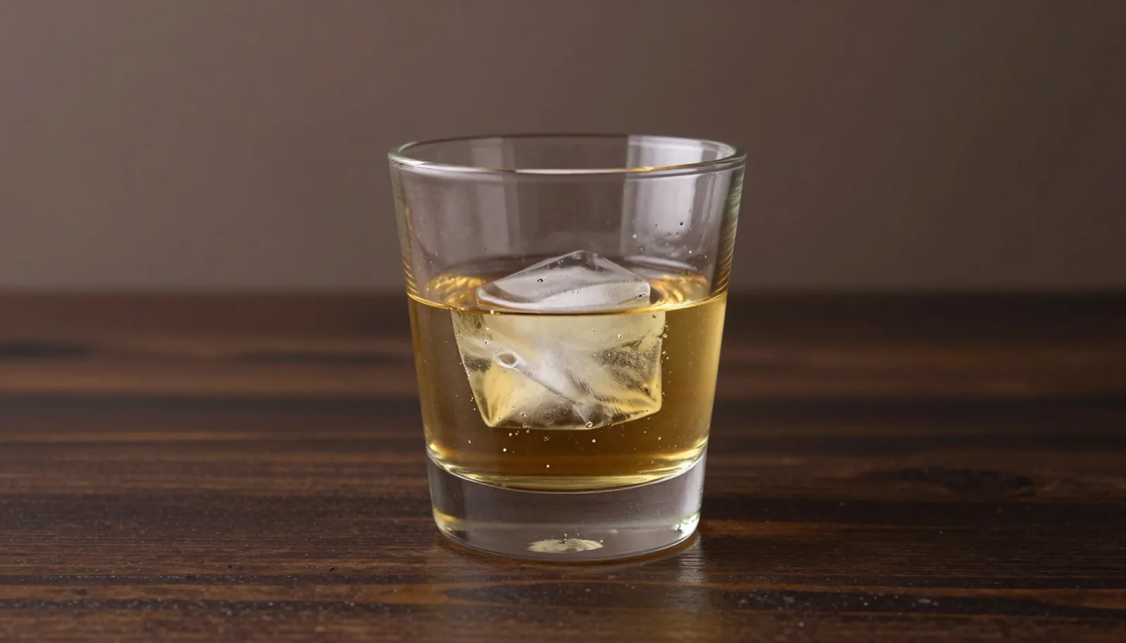 Ly whisky pha trộn màu vàng với một viên đá lớn trên bàn gỗ