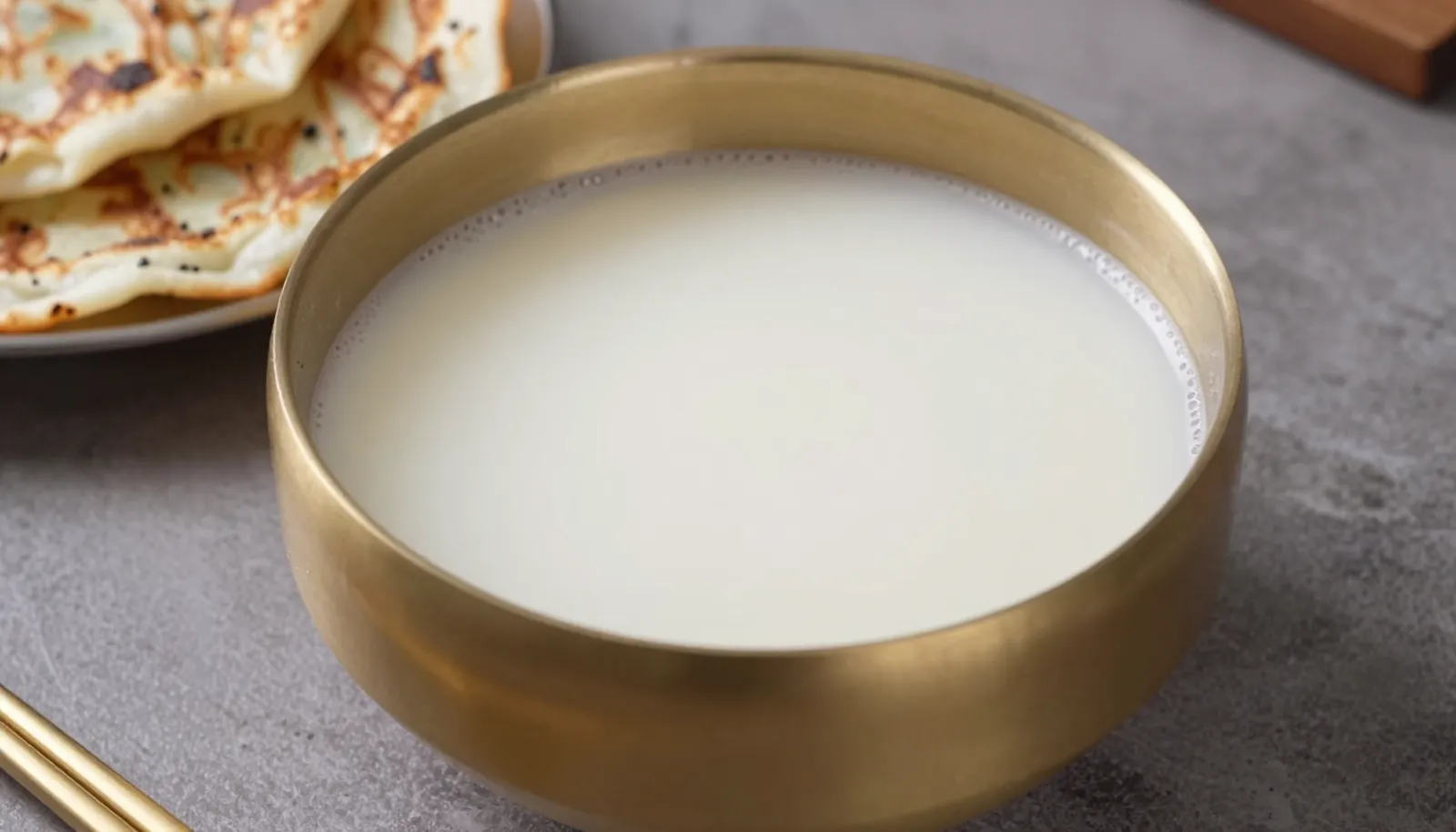Bát đồng đựng makgeolli trắng đục bên bánh xèo Hàn Quốc