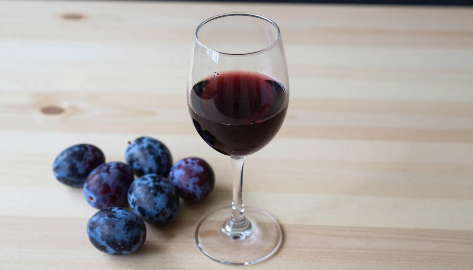 Ly vang Merlot màu hồng ngọc bên những quả mận chín