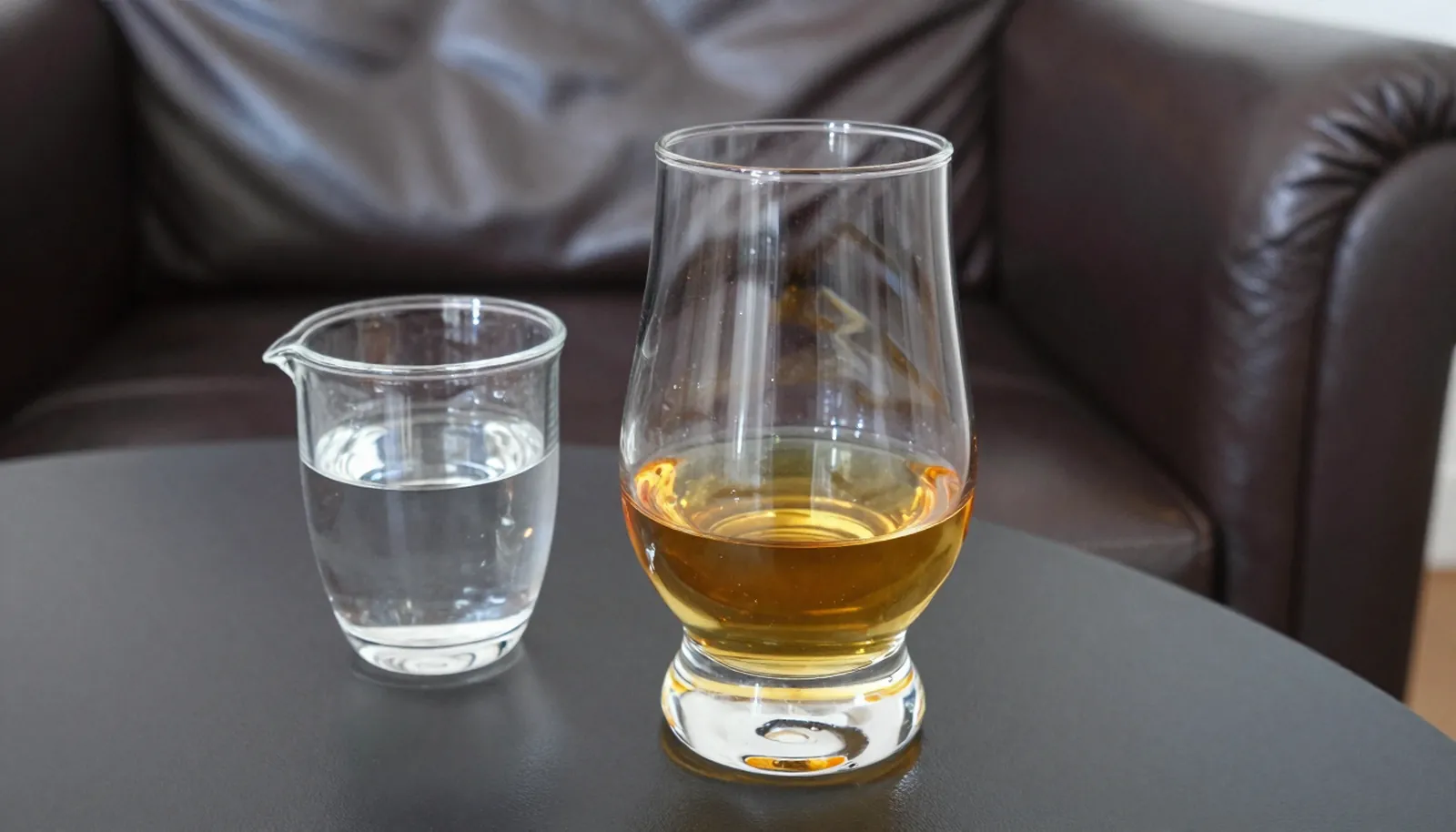 Ly single malt bên bình nước nhỏ trên bàn cạnh ghế da